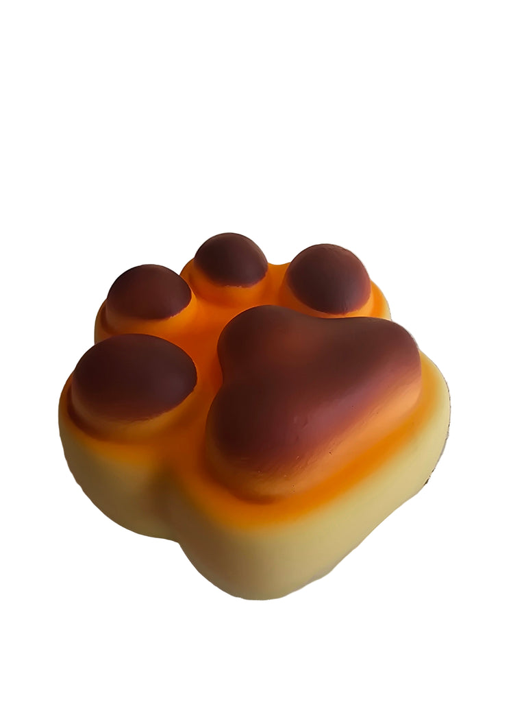 Yellow and brown paw-shaped squishy toy next to a box labeled 'Squishy' on a textured surface.